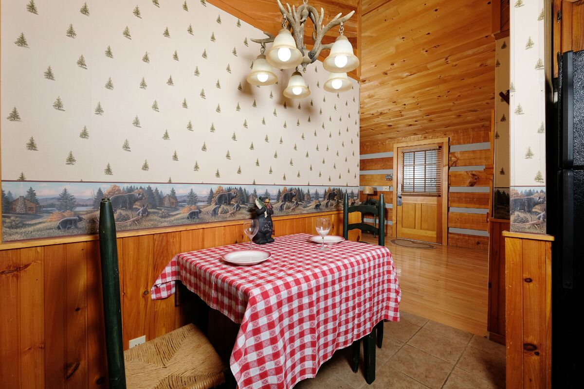 A wooden cabin interior with a dining table set for two, a chandelier, and a mural on the wall.