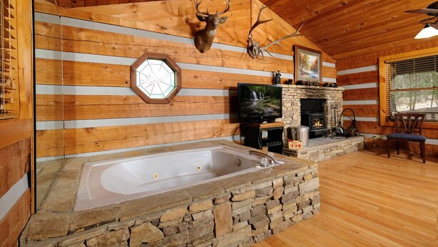 A log cabin interior with a stone fireplace, a stone bathtub, wooden walls, and a mounted deer head. - Gettin' Lucky: Hit the Jackpot in the Smokies (Pigeon Forge)