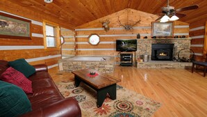 A log cabin interior with a leather couch, a stone fireplace, a television, and a ceiling fan. - Gettin' Lucky: Hit the Jackpot in the Smokies (Pigeon Forge)