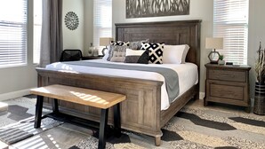 A bedroom with a large bed, a wooden bench, a nightstand, and a wall art piece. - Desert Living 5 Bedroom Home by RedAwning (Washington)