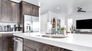A modern kitchen with dark wood cabinets, stainless steel appliances, a large island with a sink, and a flat-screen TV in the background. - Desert Living 5 Bedroom Home by RedAwning (Washington)