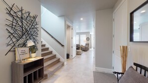 A modern hallway with a staircase, a wall-mounted abstract art piece, a welcome sign, and a minimalist decor style. - Desert Living 5 Bedroom Home by RedAwning (Washington)