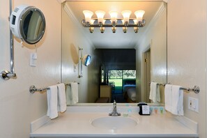 Een badkamer met een grote spiegel, een wastafel en een badkamermeubel. Handdoeken hangen aan de muur en er is een douche in de achtergrond te zien.