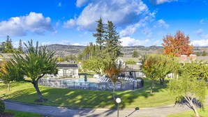 Zona residencial con piscina rodeada de sillas de descanso y una valla, con árboles y cielo despejado al fondo.