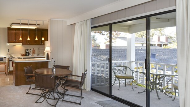 Una cocina moderna con iluminación colgante, un comedor con mesa y sillas redondas, y un balcón con mobiliario exterior.