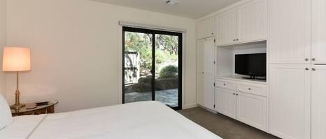 A bedroom with a bed, a TV, and a sliding glass door leading to a garden.