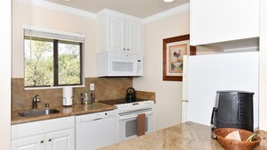 A kitchen with white cabinets, a granite countertop, a built-in microwave, a stove, a sink, and a coffee maker.