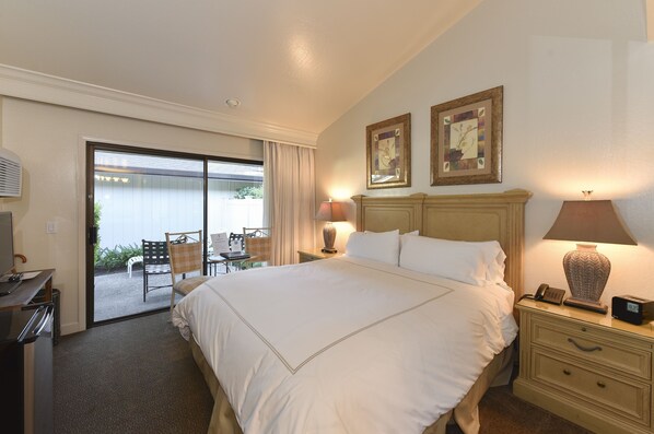 Habitación de hotel con una cama grande, dos lámparas de noche, un escritorio con teléfono, y vistas a un patio exterior con sillas y una mesa.