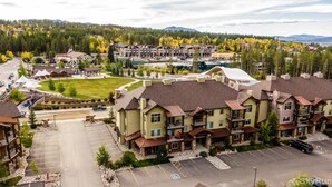 A multi-story hotel with a parking lot, surrounded by trees and a mountainous backdrop. - Trailhead Lodge One Bedroom 801 Condo by RedAwning (Winter Park)