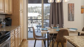 A modern kitchen with wooden cabinets, a granite countertop, and a dining area with a table set for two. - Trailhead Lodge One Bedroom 801 Condo by RedAwning (Winter Park)