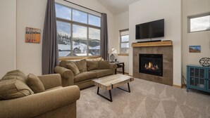 A living room with a sofa, a coffee table, a fireplace, and a television. - Trailhead Lodge One Bedroom 801 Condo by RedAwning (Winter Park)
