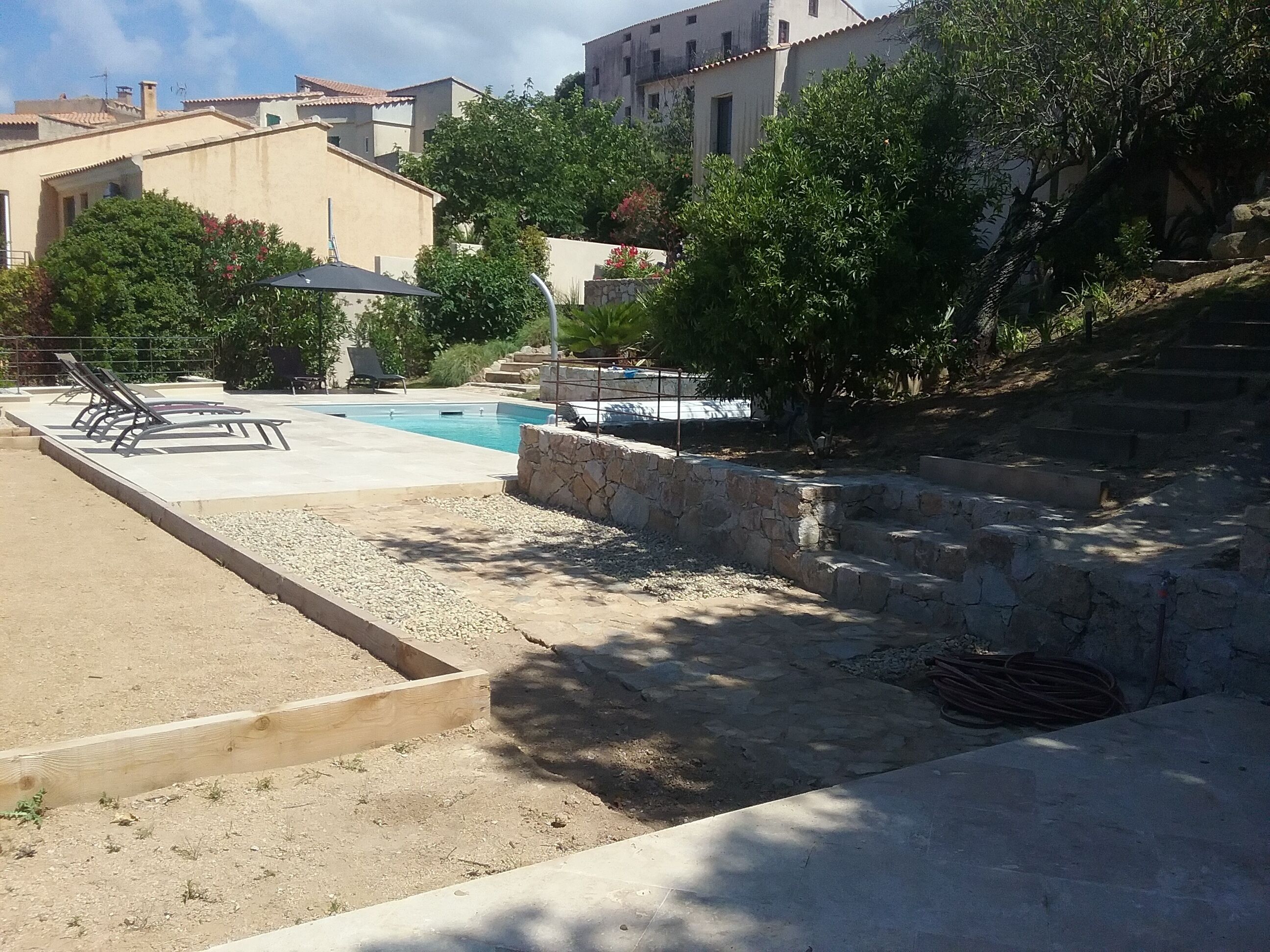 A pool area with lounge chairs, a stone wall, and steps leading up to a building.