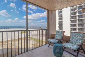 Un balcon avec vue sur la plage et l’océan, aménagé avec deux chaises et une petite table.