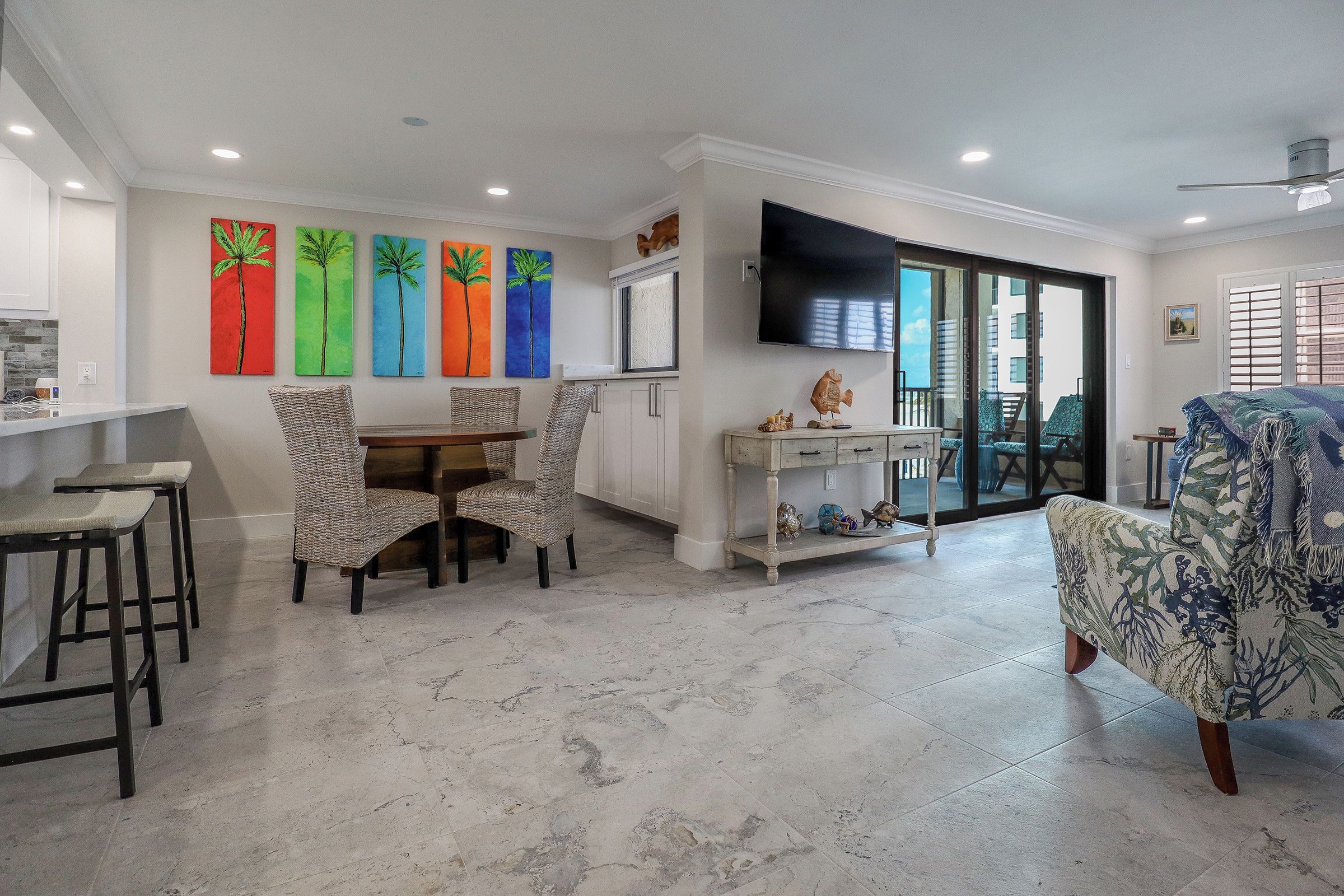 A modern living space with a dining area, a TV mounted on the wall, and a view through a sliding glass door.