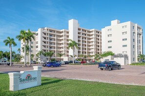 A multi-story hotel with a parking lot in front, palm trees, and a sign for Sandarac Condominiums.