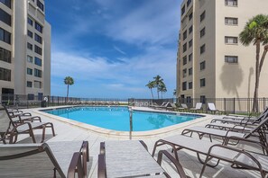 A swimming pool with lounge chairs and palm trees, surrounded by high-rise buildings.