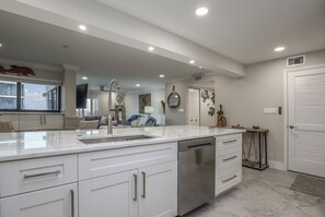 A modern kitchen with white cabinetry, a stainless steel dishwasher, and a large island with a sink. - World Class Sunsets on the Gulf From Your Lanai! Beachfront 2B/2B Sandarac Vacation Condo (Fort Myers Beach)