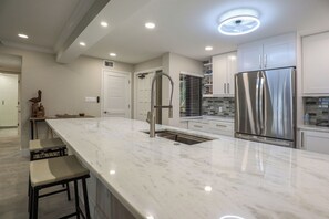 A modern kitchen with a marble countertop, stainless steel appliances, and recessed ceiling lighting. - World Class Sunsets on the Gulf From Your Lanai! Beachfront 2B/2B Sandarac Vacation Condo (Fort Myers Beach)