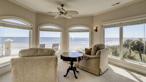 A room with a ceiling fan, a round table, two armchairs, and large windows offering a view of the beach. - 81 Dune Lane - Oceanfront 6BR | Private Pool & Spa | Sleeps 18 (Hilton Head Island)