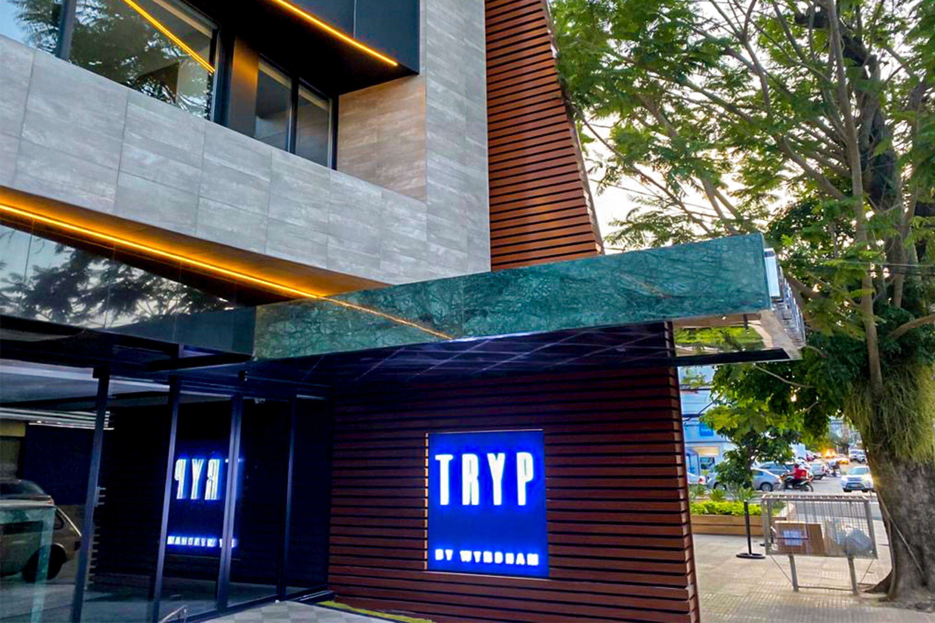 A modern building with a prominent 'TRYP' sign, large windows, and a tree in the background.