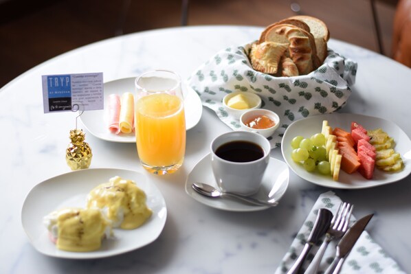 Une table dressée pour le petit-déjeuner, avec des œufs, des toasts, des fruits, du jus, du café et divers condiments.