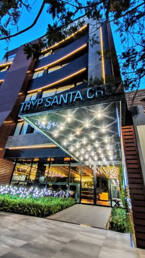 Ein modernes Gebäude mit dem Schild "TRYP SANTA CRUZ" und einem Glastürdurchgang mit dekorativer Beleuchtung.