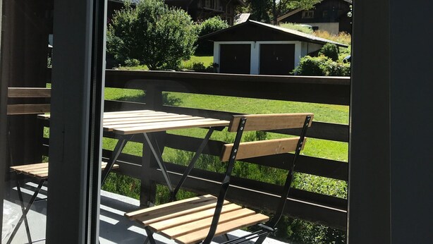 Un balcon avec une table et des chaises en bois, donnant sur un paysage montagneux parsemé de maisons et de verdure.