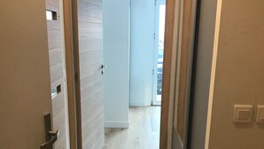 Un couloir doté d’un plancher en bois et d’une porte donnant sur une pièce avec une grande fenêtre.