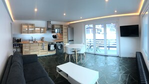Un espace de vie compact comprenant un coin cuisine, un coin repas et un espace détente avec un canapé et une table.