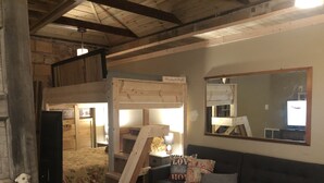 Un accogliente soggiorno con un divano scuro, un tavolino in vimini e una scala in legno che conduce a una camera da letto soppalcata.