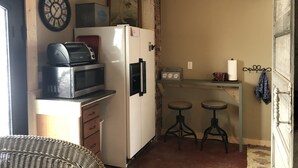 Una cucina compatta con forno a microonde, tostapane e frigorifero. Ci sono due sgabelli e un tavolino.