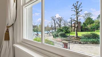 A window with a view of a park, a body of water, and a brick building.