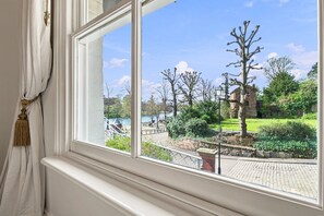 A window with a view of a park, a body of water, and a brick building. - Beautiful period cottage, exceptional riverside location in the heart of Chester (Chester)