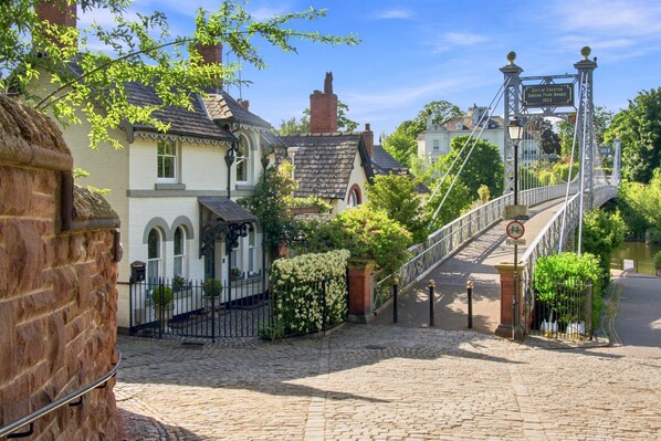 A cobblestone street leading to a bridge with a sign indicating the Queens Park Bridge.