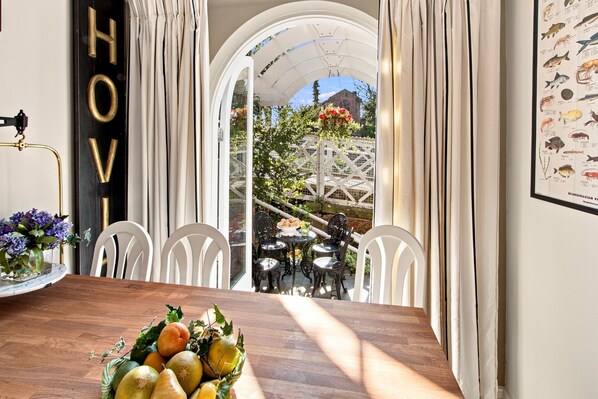 A dining area with a wooden table, white chairs, and a view through an arched window to a garden. - Beautiful period cottage, exceptional riverside location in the heart of Chester (Chester)