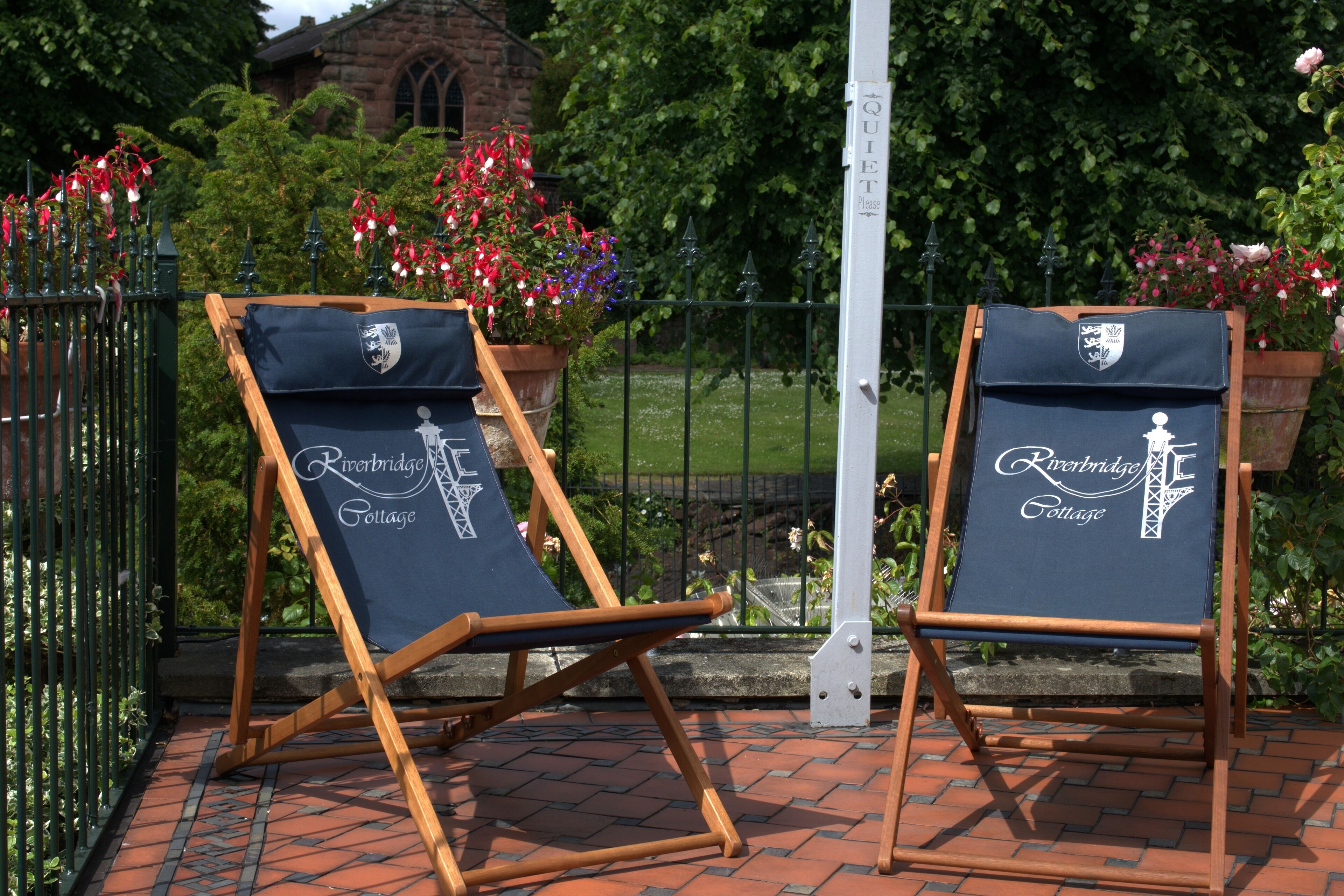 Two Riverbridge Cottage branded easels on a brick patio with a metal fence and greenery in the background.