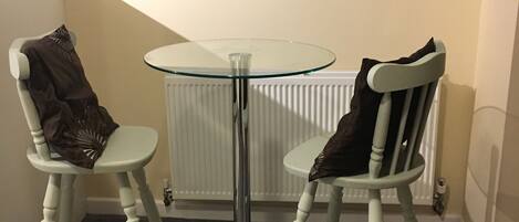 Une petite pièce avec deux chaises blanches et une table dont le plateau est en verre.