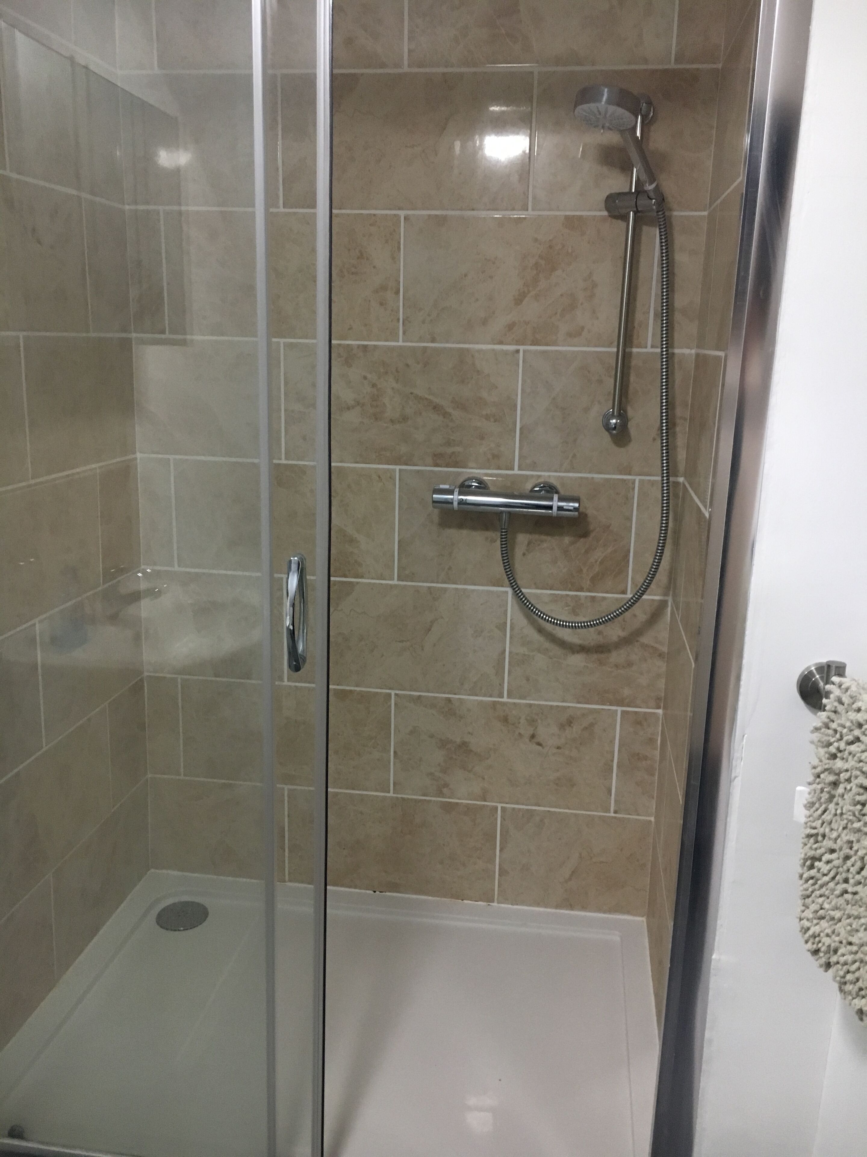 Un vestidor de ducha con paredes de vidrio, con cabezal de ducha de mano y grifo empotrado.