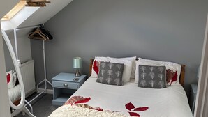 Ein Schlafzimmer mit Bett, Nachttisch, Kommode, Heizkörper, Pendelleuchte und Deckenventilator.
