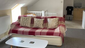 Ein gemütliches Schlafzimmer im Loft-Stil mit einem rot-weiß karierten Sofa, einem weißen Couchtisch und einer schrägen Decke mit Dachfenstern.