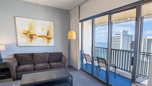 A modern hotel room with a large sliding glass door leading to a balcony with a city view.