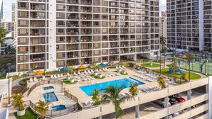 A multi-story hotel with a rooftop pool, lounge chairs, and a parking garage.