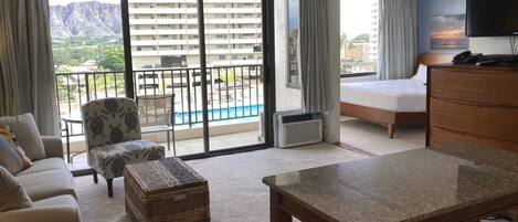 A hotel room with a balcony, a bed, a TV, a desk, and a chair.