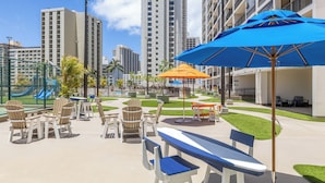 A patio area with outdoor seating, a pool, and high-rise buildings in the background. - Deluxe Condo , Free Parking & Wi-Fi (Honolulu)