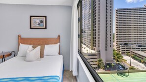 Ein Hotelzimmer mit einem Bett, einem gerahmten Bild an der Wand und Blick auf ein hohes Gebäude sowie einen Tennisplatz.