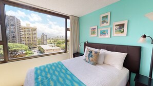 Una habitación de hotel con un ventanal grande, una cama con colcha estampada, cabecero marrón y cuadros en la pared.
