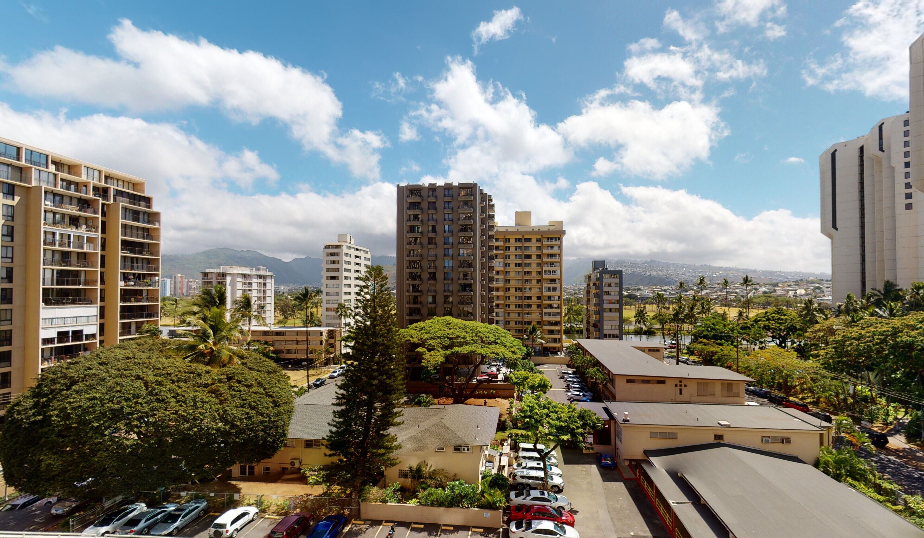 Zona residencial con edificios de apartamentos de varios pisos, un estacionamiento y vistas a montañas distantes.