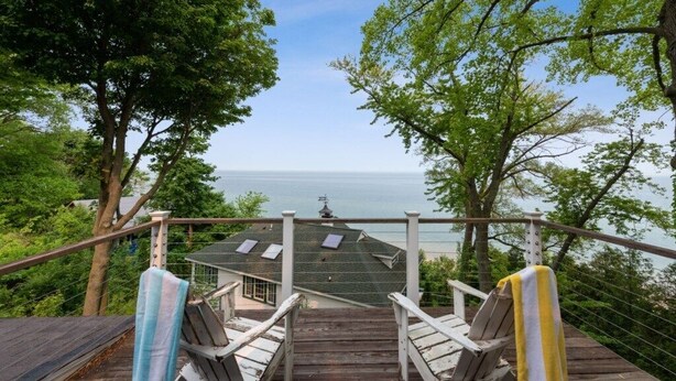 Une terrasse en bois avec deux chaises et une table, d’où l’on peut admirer un plan d’eau et, au loin, une maison avec un toit vert.