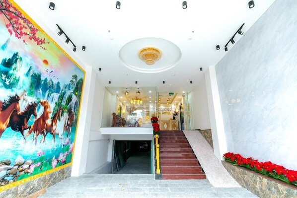 A hotel lobby with a staircase, a mural, and a chandelier. - Hata hotel (Quy Nhon Nam)