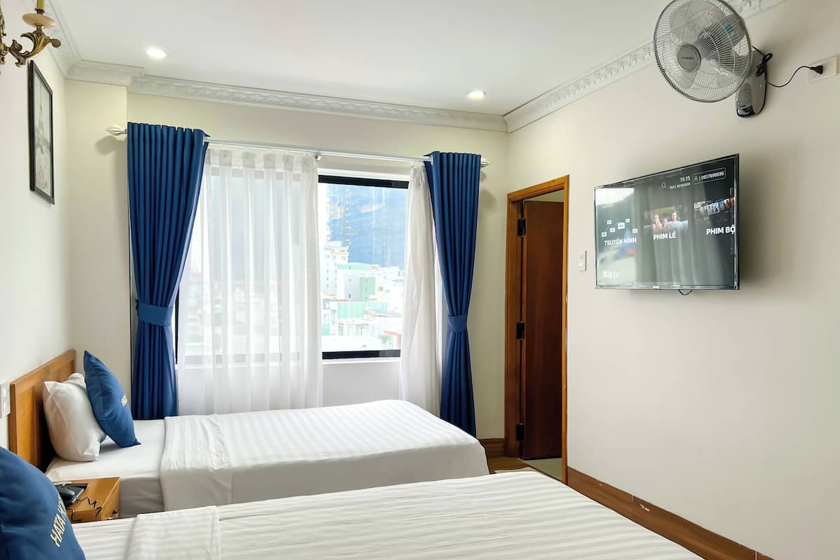 A hotel room with two beds, a TV on the wall, and a window with curtains.